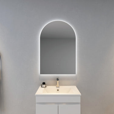 Bathroom vanity with a white cabinet and illuminated arch-shaped mirror on a gray wall.